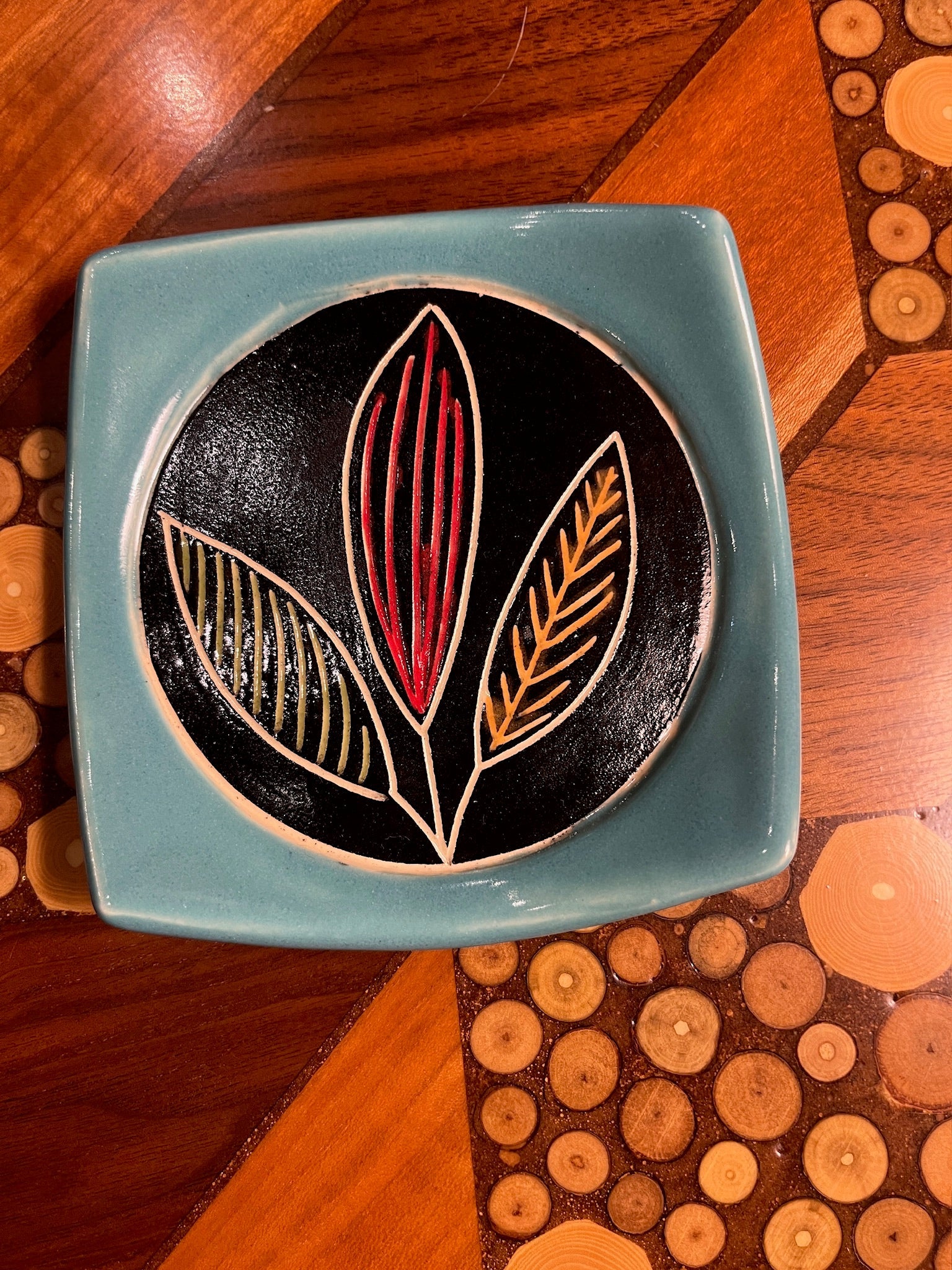 Ceramic tile with leaf design on a wooden surface