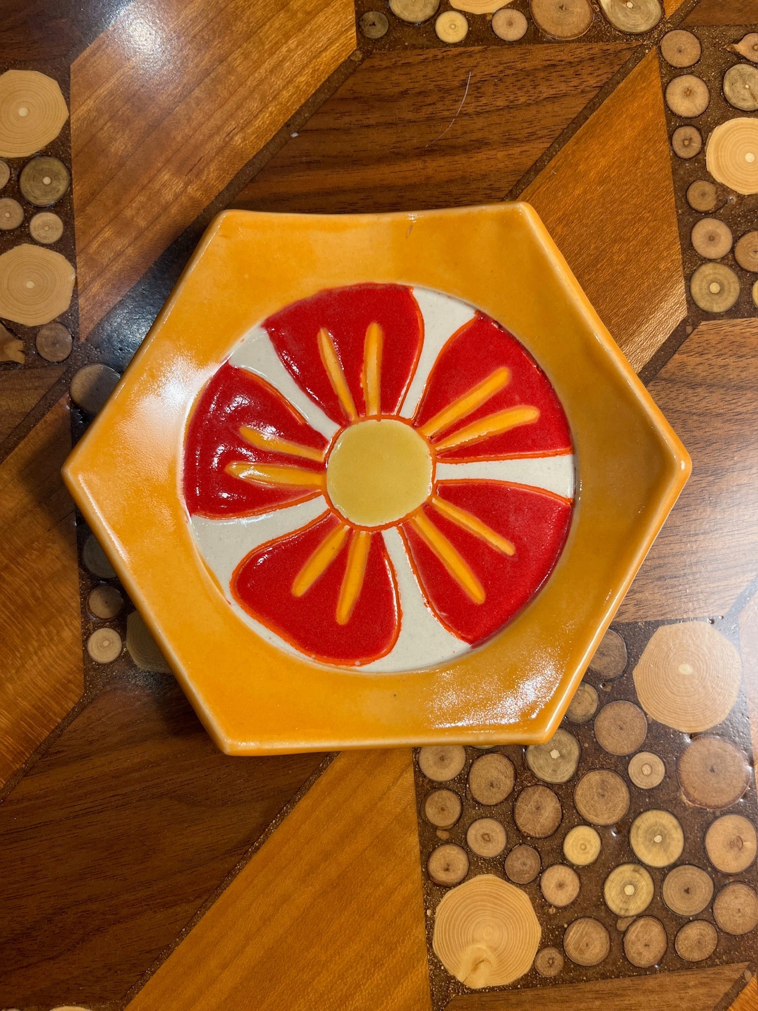 Hexagonal ceramic plate with a red and yellow design on a wooden surface
